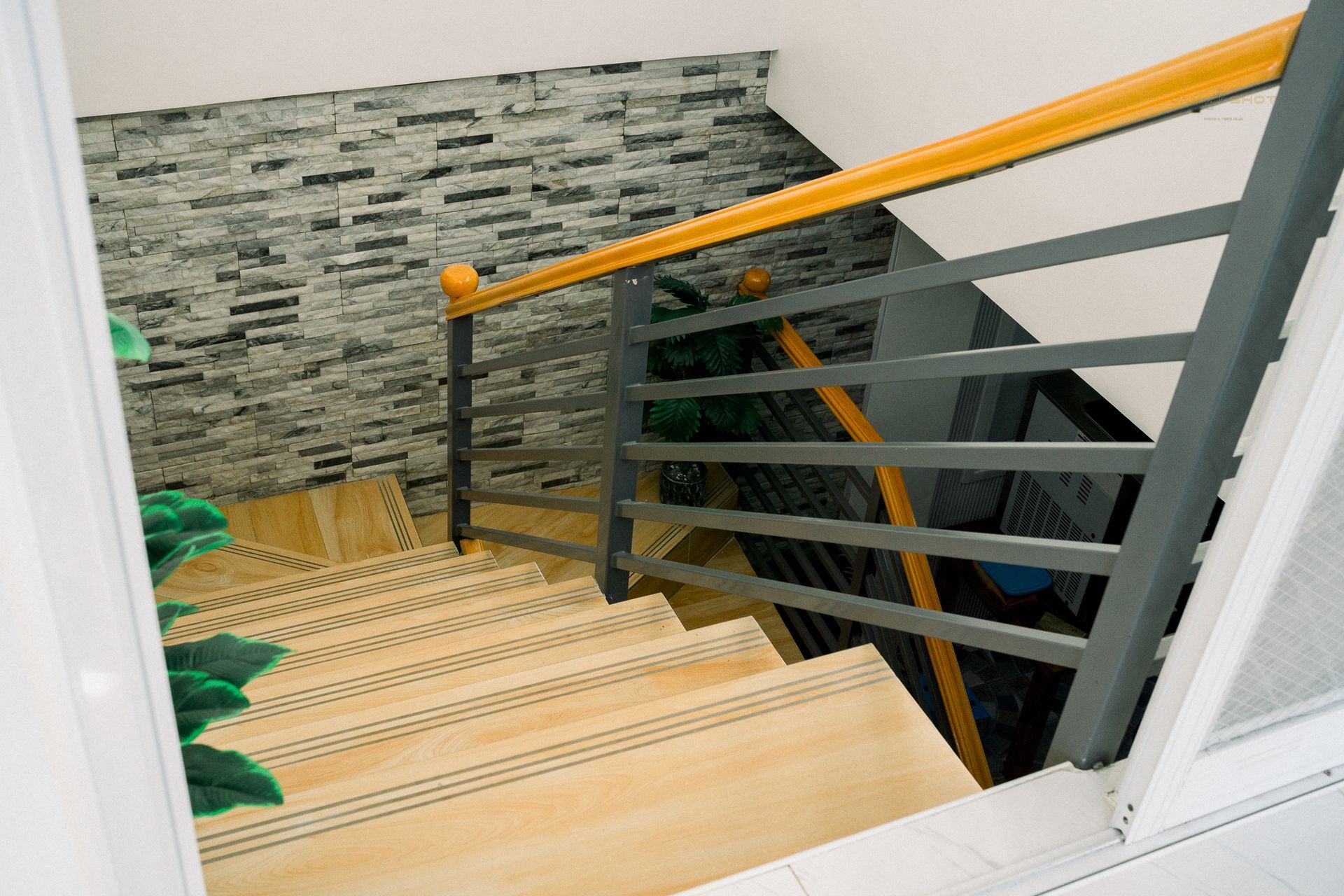 A staircase with light wood steps, gray metal railings, a yellow handrail, and a stone-textured wall.