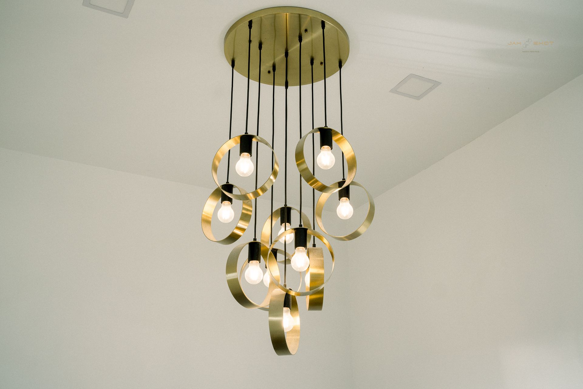 A brass, multi-pendant chandelier features circular frames surrounding exposed light bulbs hanging from a circular mount.