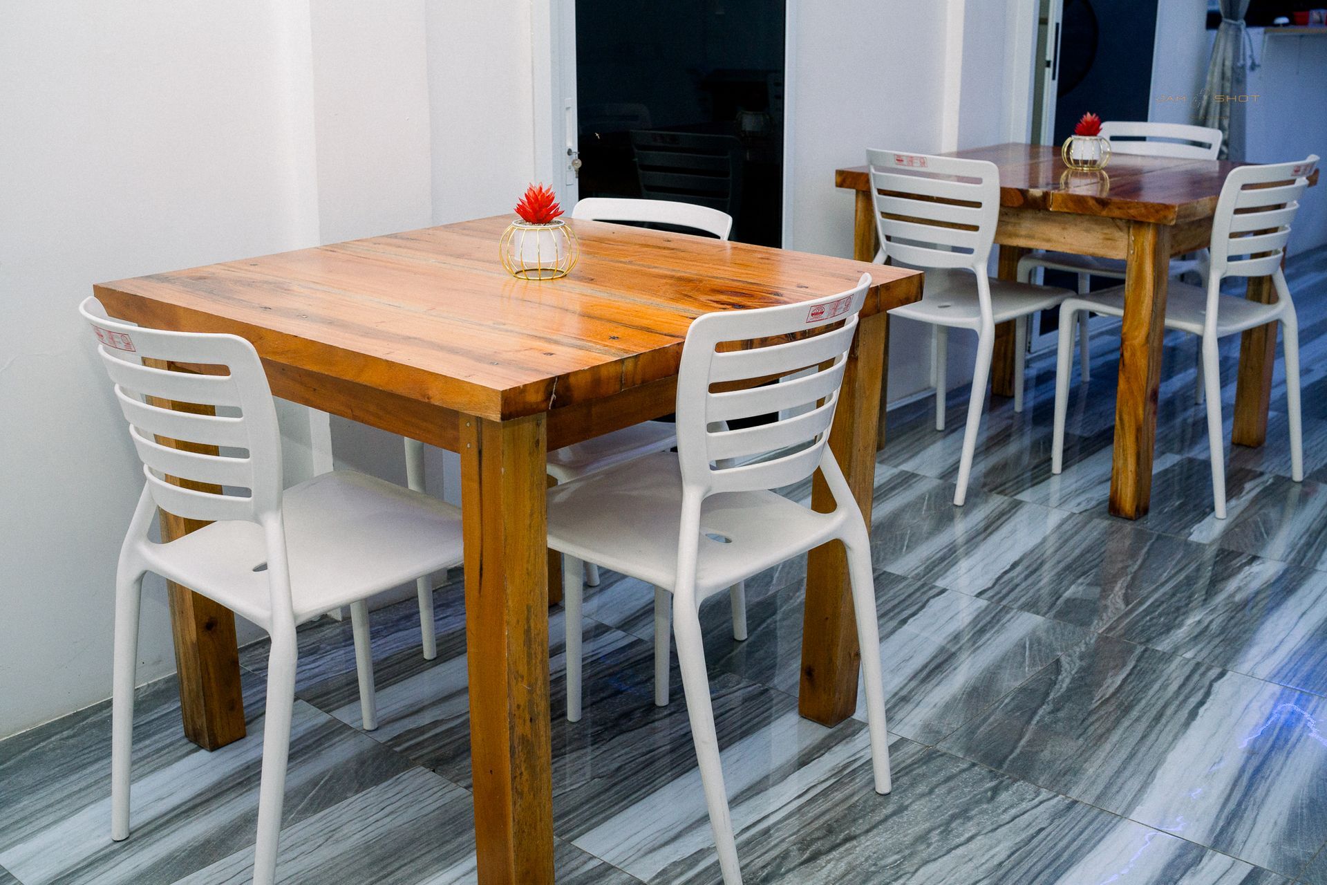 Two square wooden tables with white chairs arranged on a grey tiled floor in a dining area.
