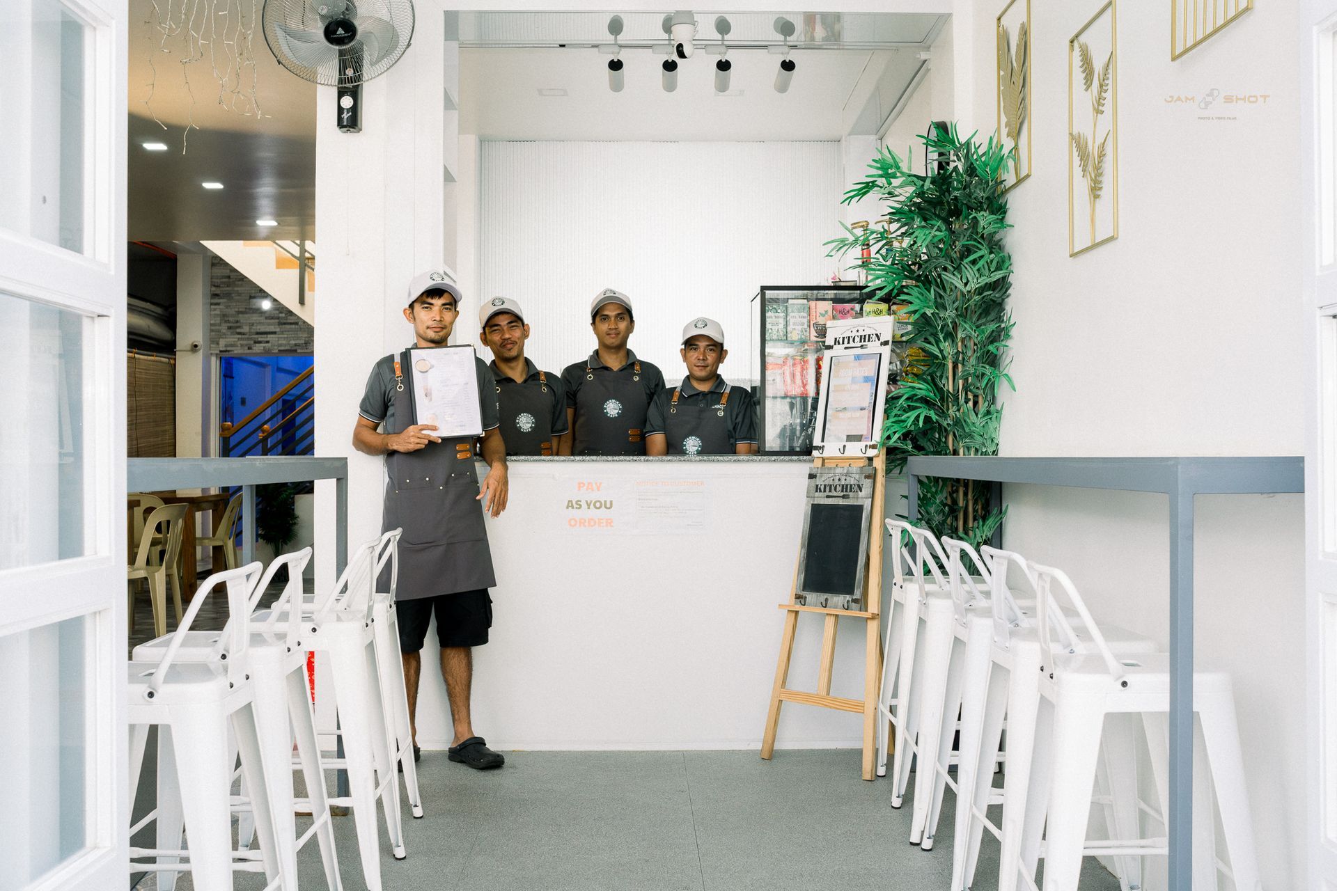 Four employees in grey shirts stand behind a white counter inside a bright, minimalist café with white stools.