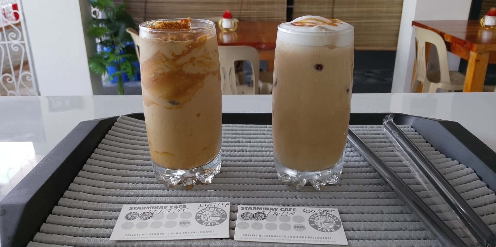 Two tall glasses of iced coffee topped with foam, sitting on a tray with two loyalty cards and straws at a cafe table.