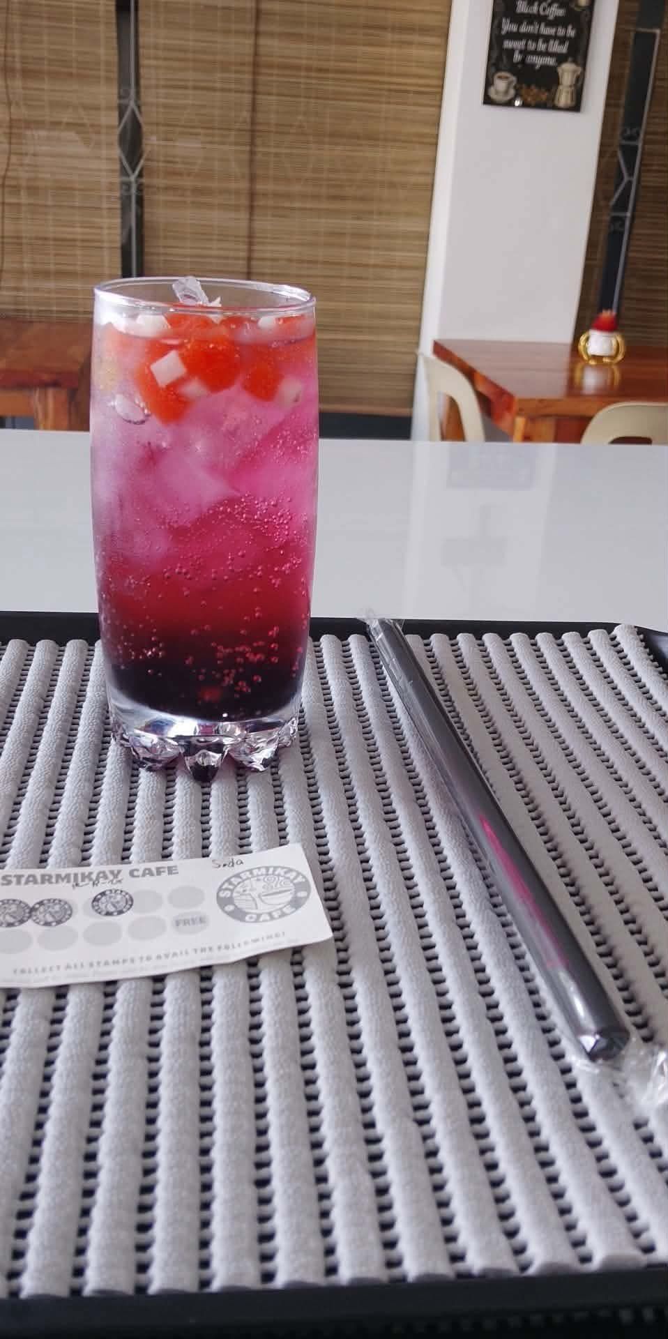 A tall, iced pink and purple gradient drink with berries on top, served with a straw on a grey textured mat.