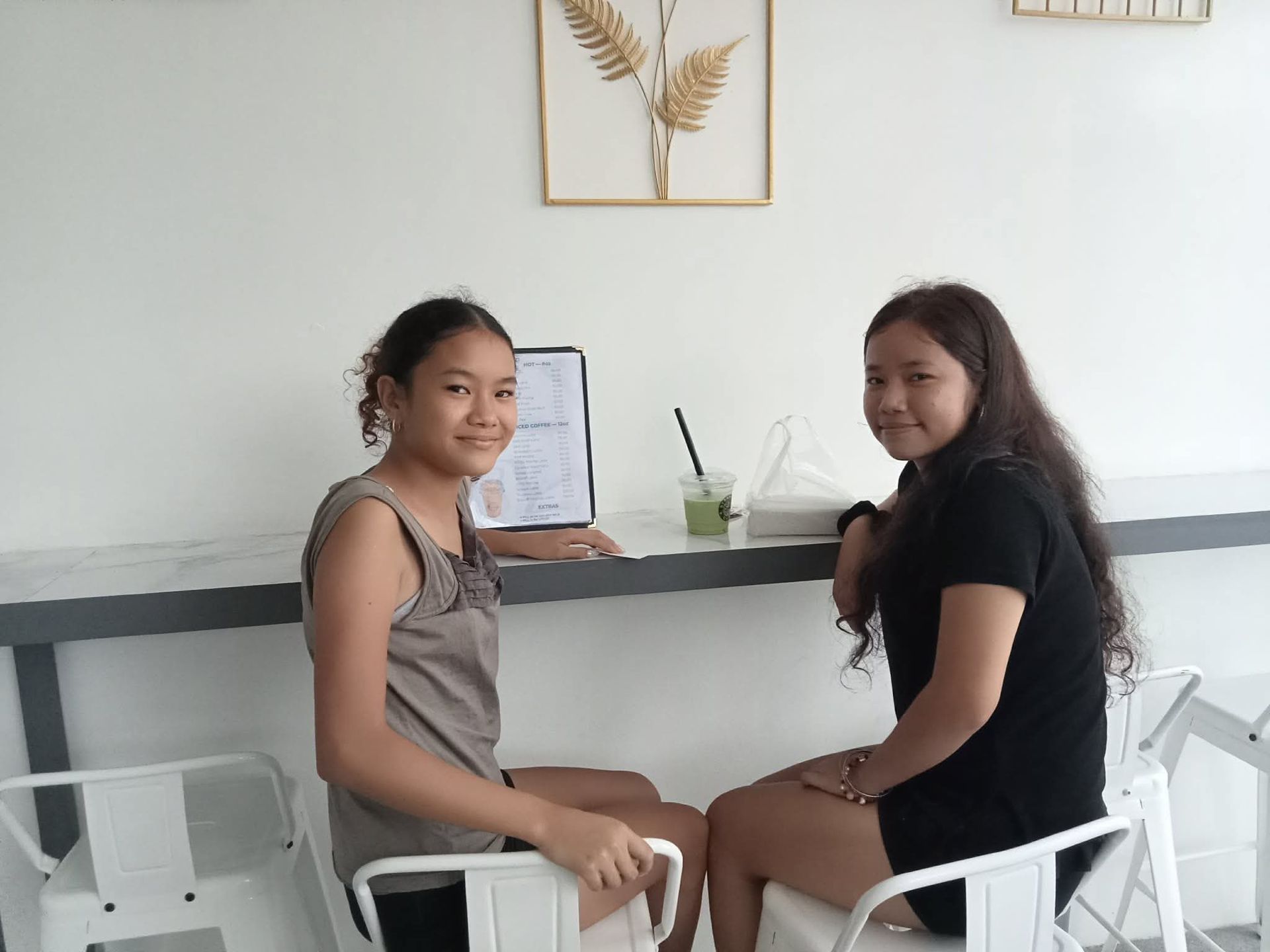 Two people sitting at a cafe table with a beverage and a menu, smiling toward the camera.