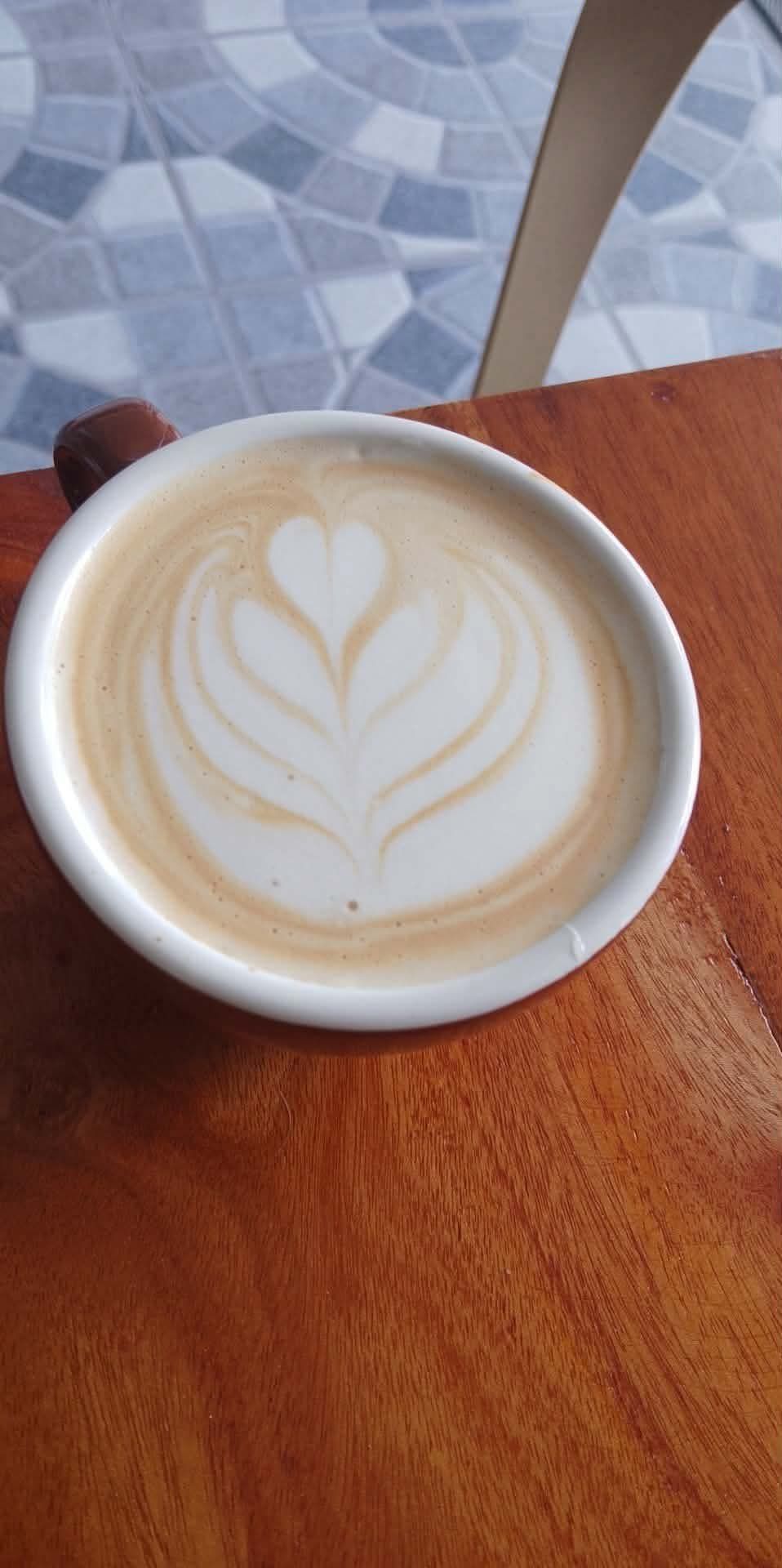 A latte with intricate heart-shaped rosetta latte art in a white ceramic mug, sitting on a wooden table.