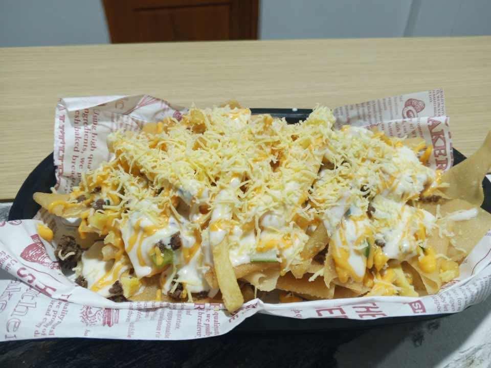 A tray of loaded french fries topped with melted cheese, a creamy white sauce, and shredded cheddar on branded paper.