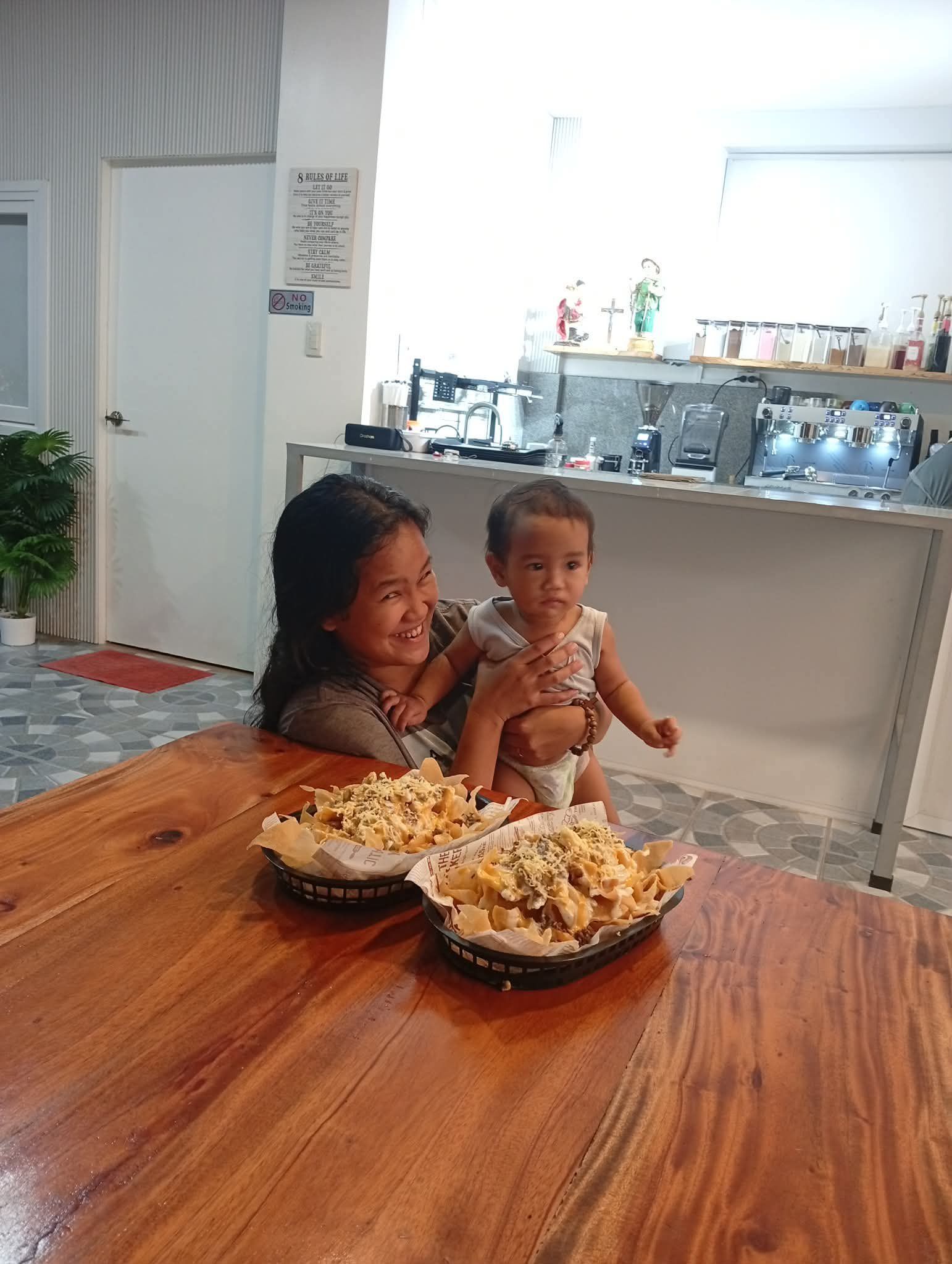 A person holding a child behind a table with two baskets of fried food in a brightly lit indoor space.