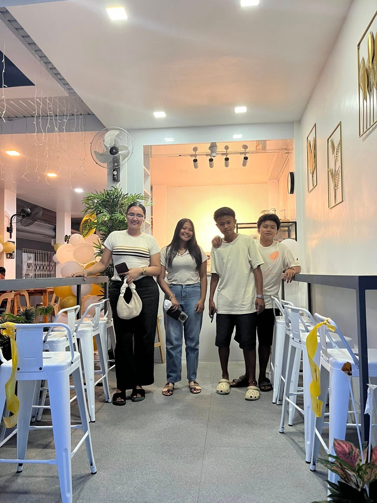 Four people stand inside a brightly lit restaurant with white furniture, smiling for a photo.