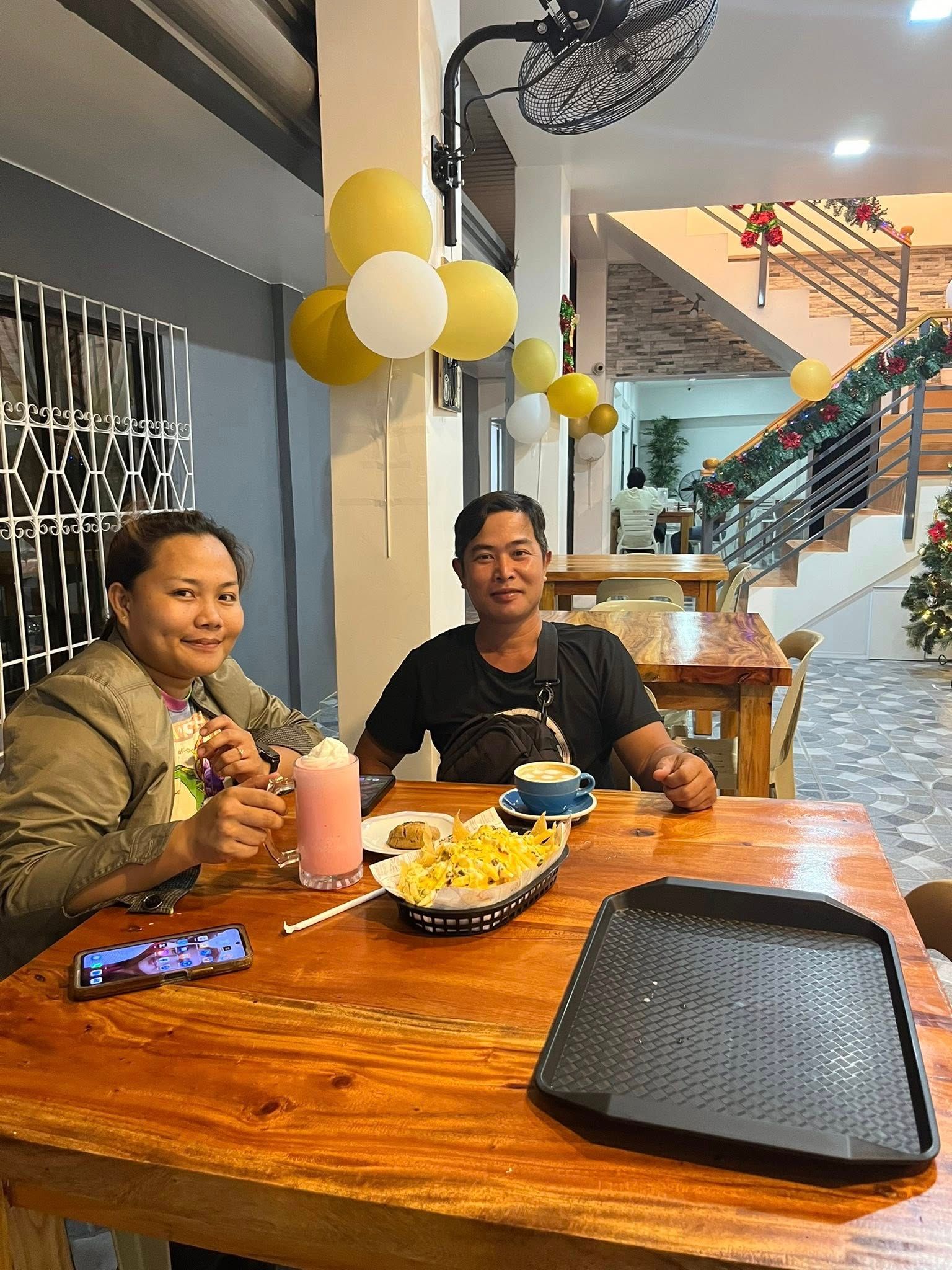 Two people smile at a table with drinks and snacks in a decorated, festive room with balloons.