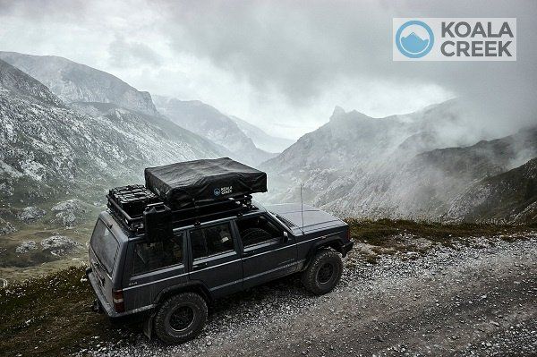 Een jeep met daarop een tent staat geparkeerd op de top van een berg.