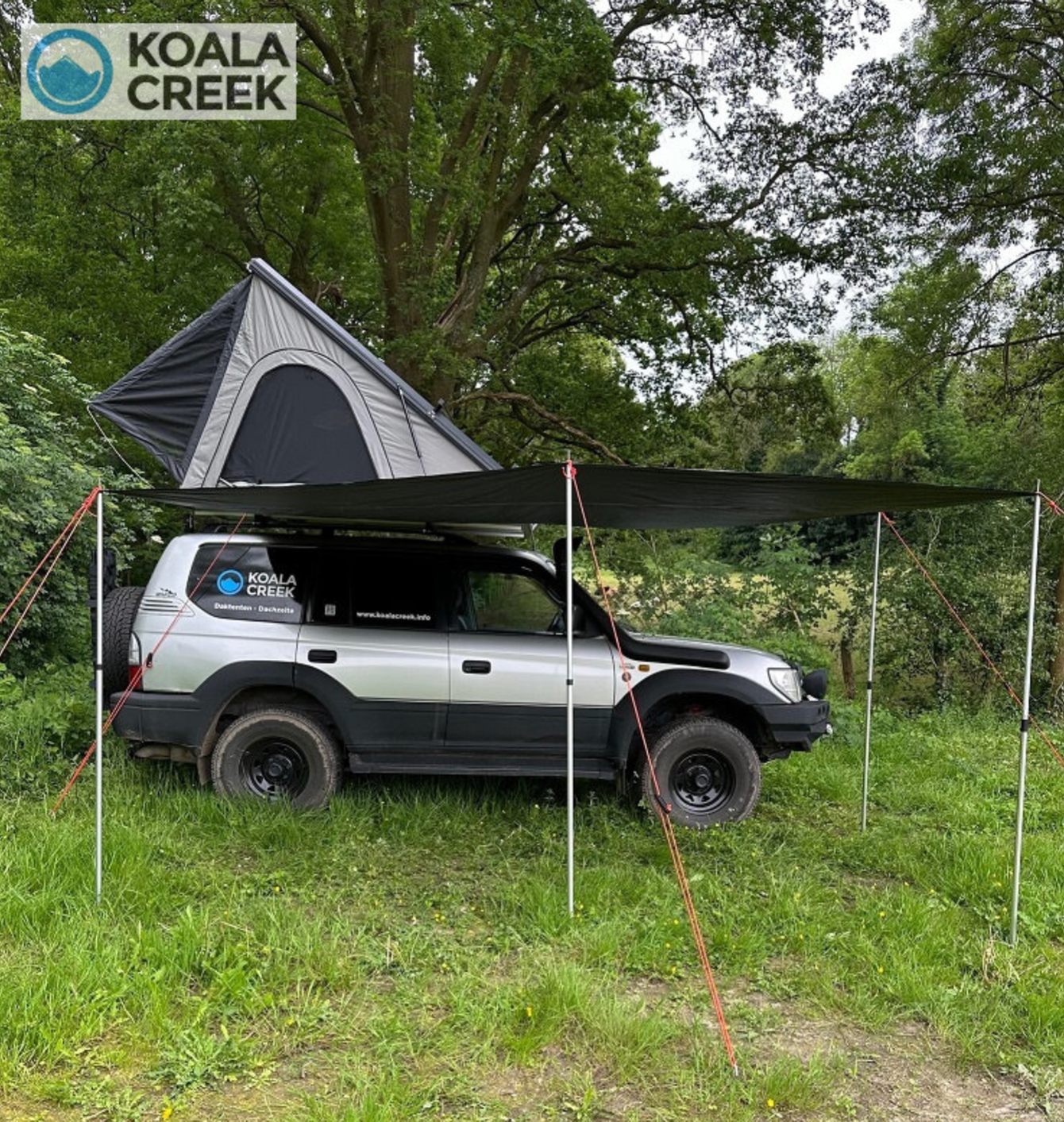 Een Toyota landcruises met een daktent erop staat geparkeerd in een grasveld.