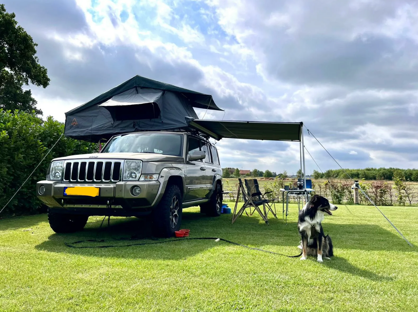 Een jeep met een tent erop staat geparkeerd in een grasveld.