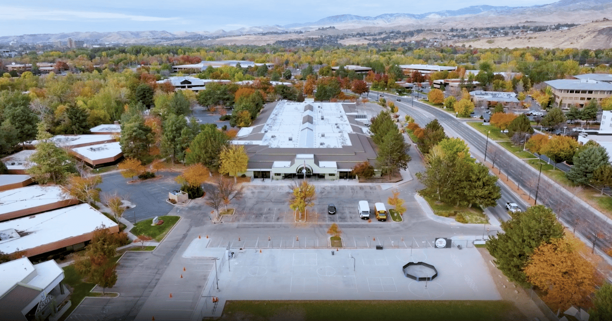 Aerial view of a commercial building with a parking lot surrounded by trees, in a town during autumn.