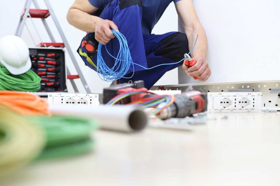 Person kneeling on the floor organizing blue electrical wires beside tools and a power strip