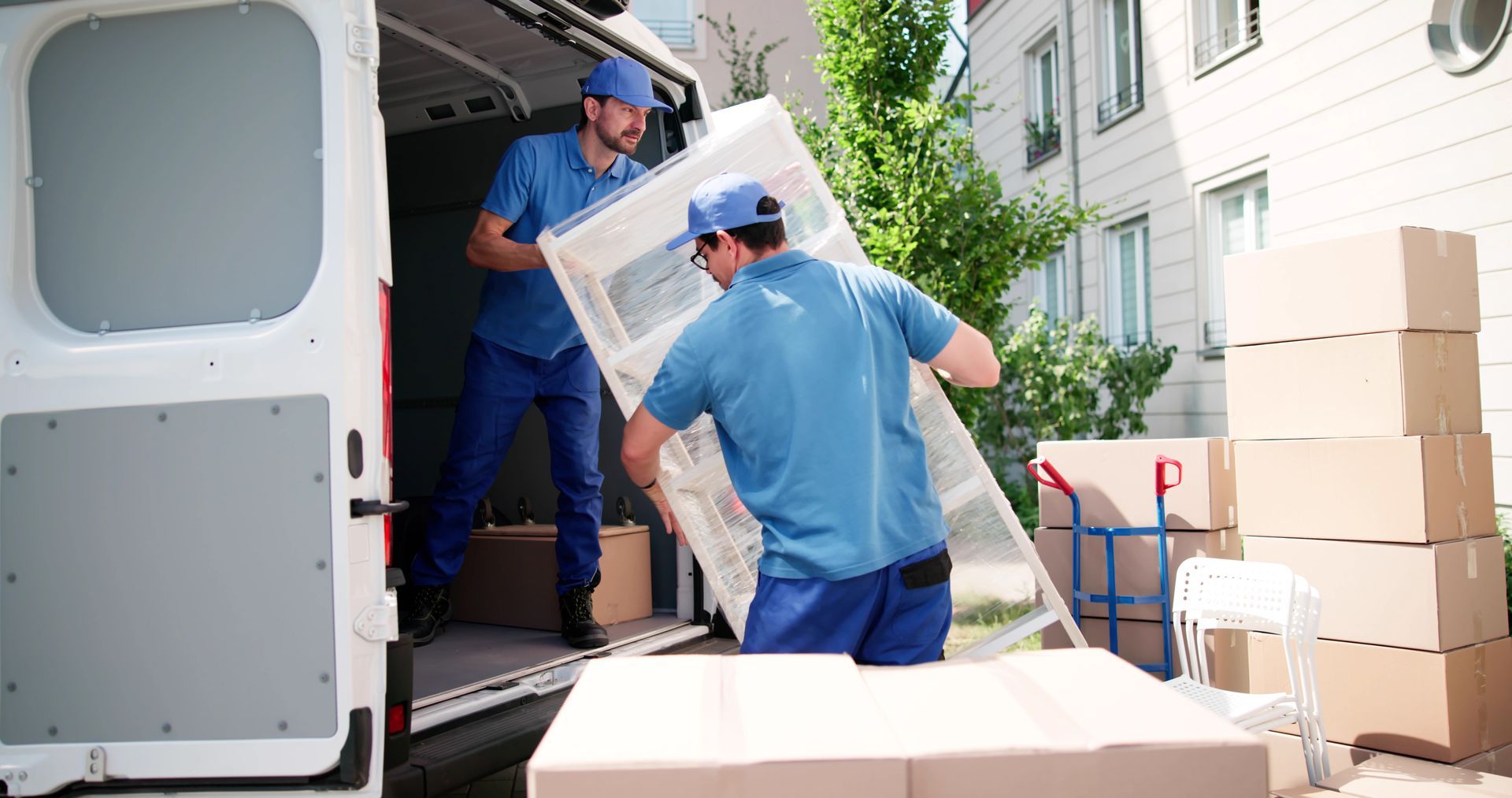 Two movers in blue uniforms loading a large white framed door into a van.