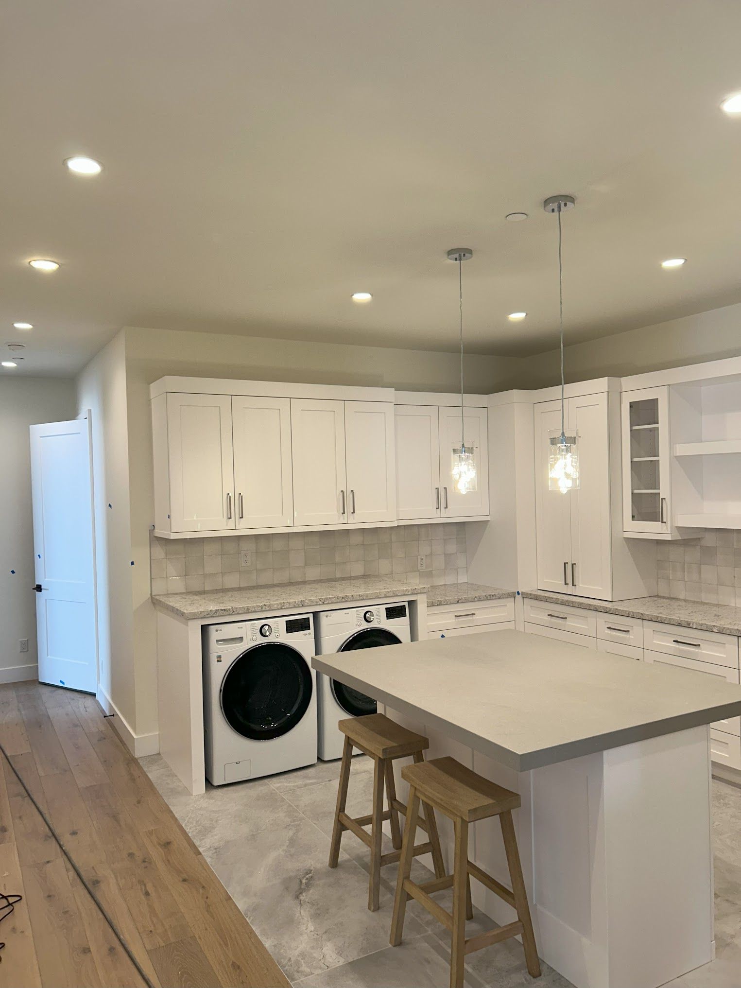 A kitchen with white cabinets , a washer and dryer , and a large island.