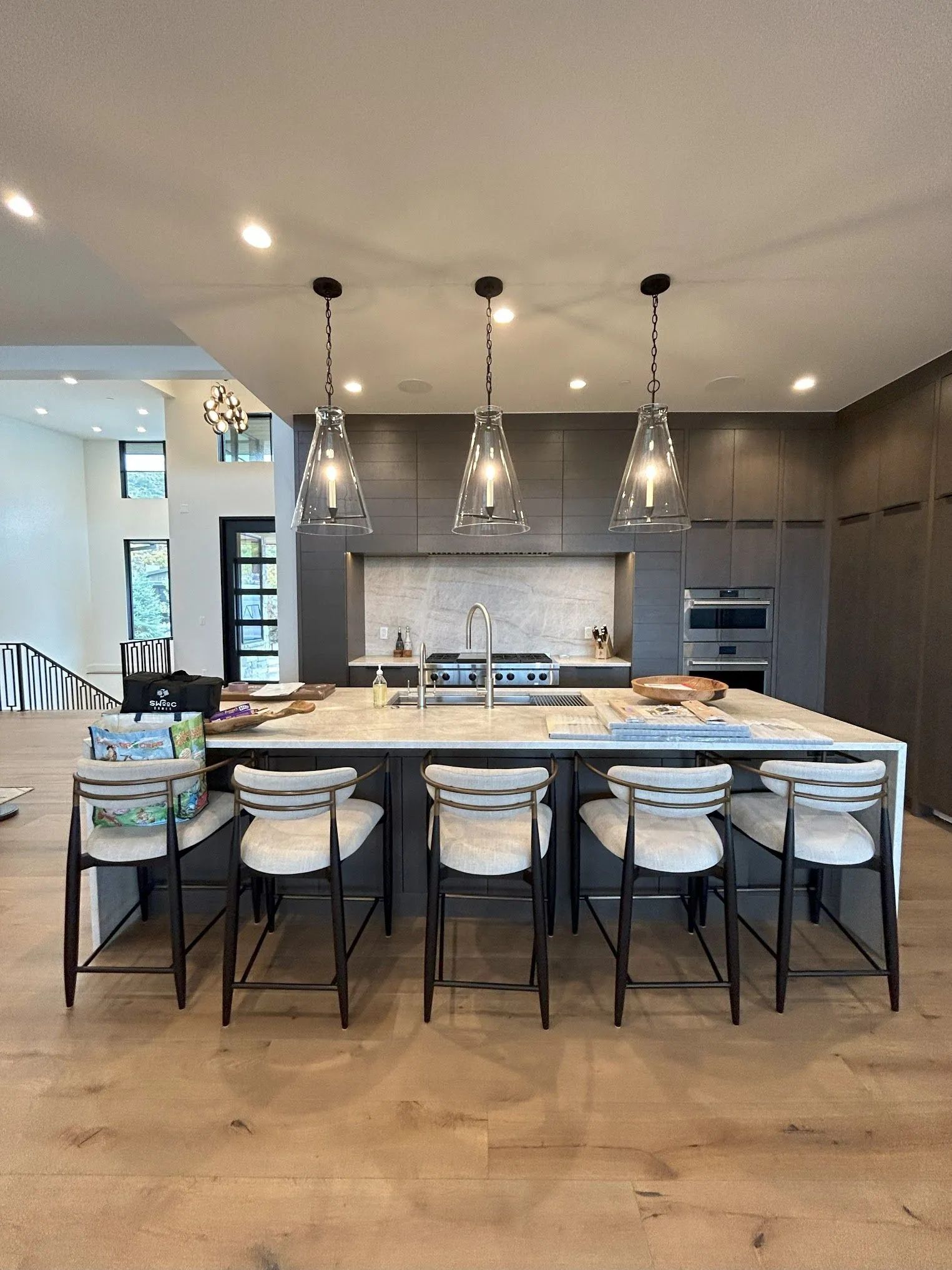 Modern kitchen with island, pendant lights, and bar stools. Dark gray cabinets and light countertops.