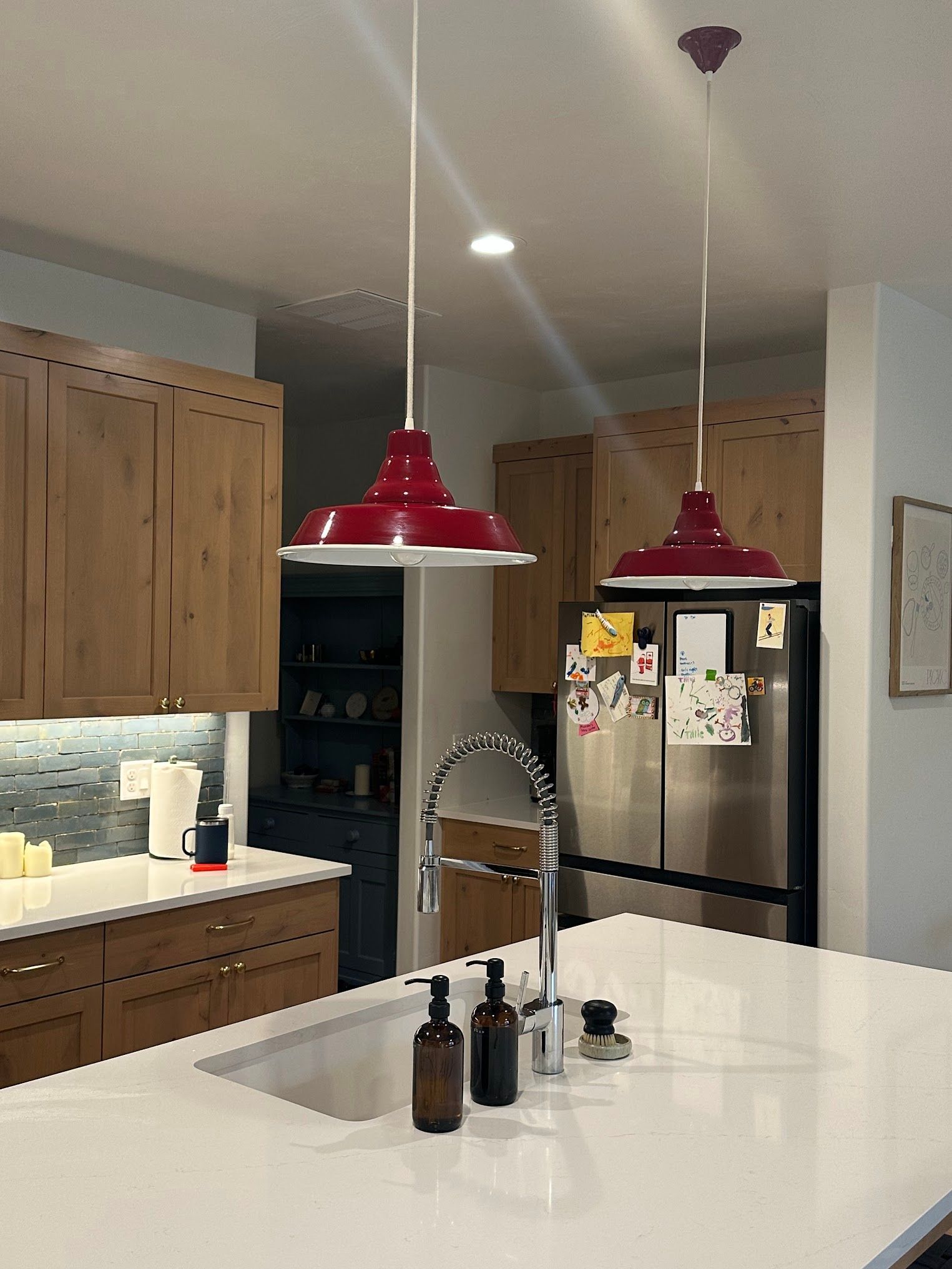 A kitchen with a sink , refrigerator , and two red lights hanging from the ceiling.