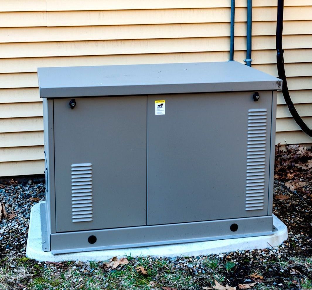Gray generator box mounted on concrete pad next to a building.