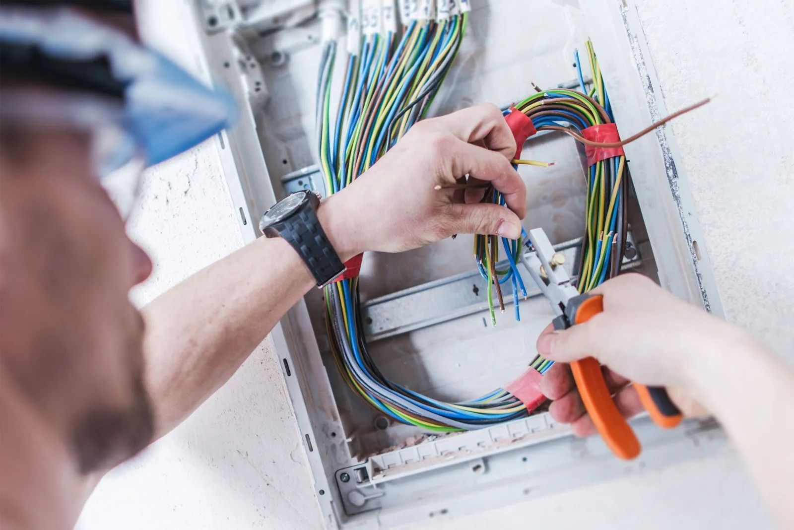 Technician wiring an electrical panel with colorful cables and orange pliers