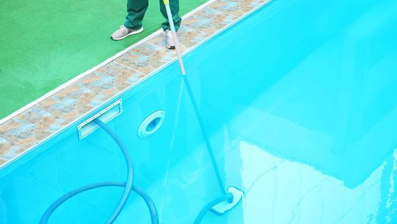 A man is cleaning a swimming pool with a mop and hose.