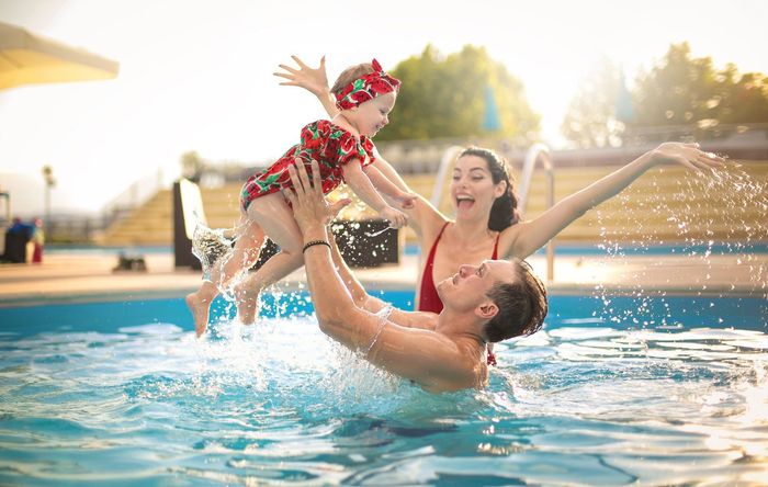 A man and woman are holding a baby in a swimming pool.