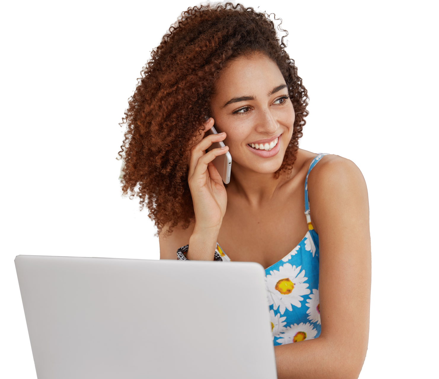 Mujer sonriendo, hablando por teléfono, mirando hacia un lado y sentada frente a una computadora portátil.