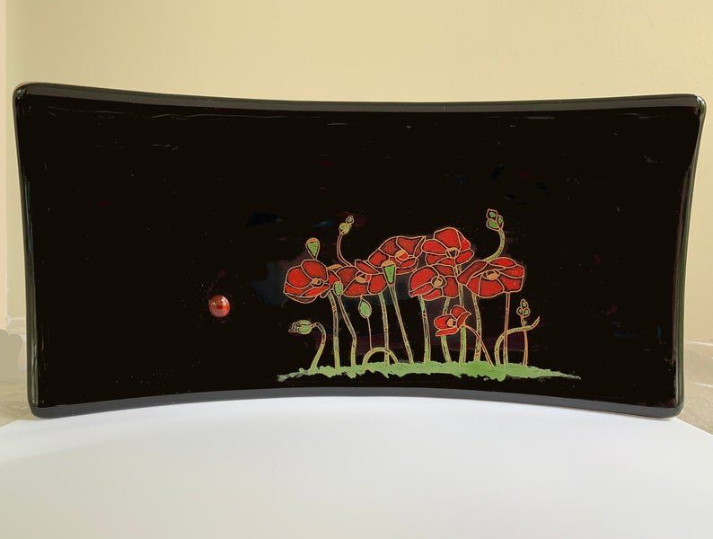 a black glass plate with a painting of red flowers and a lady bug on it