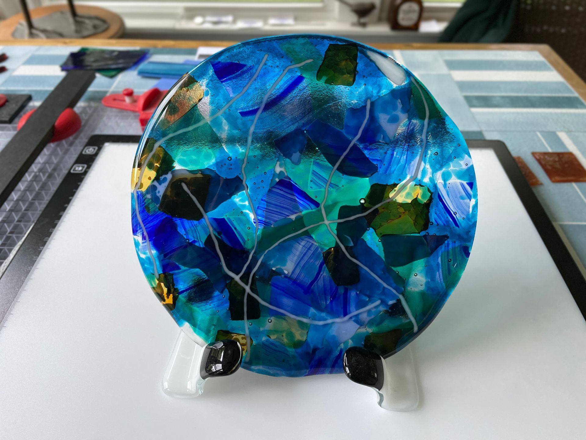 Various blues boiled to a round glass disk sitting on a fused glass stand.