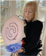 Nancy Sheridan, Glass Artist  is Next to her kiln holding a a piece of fused glass 