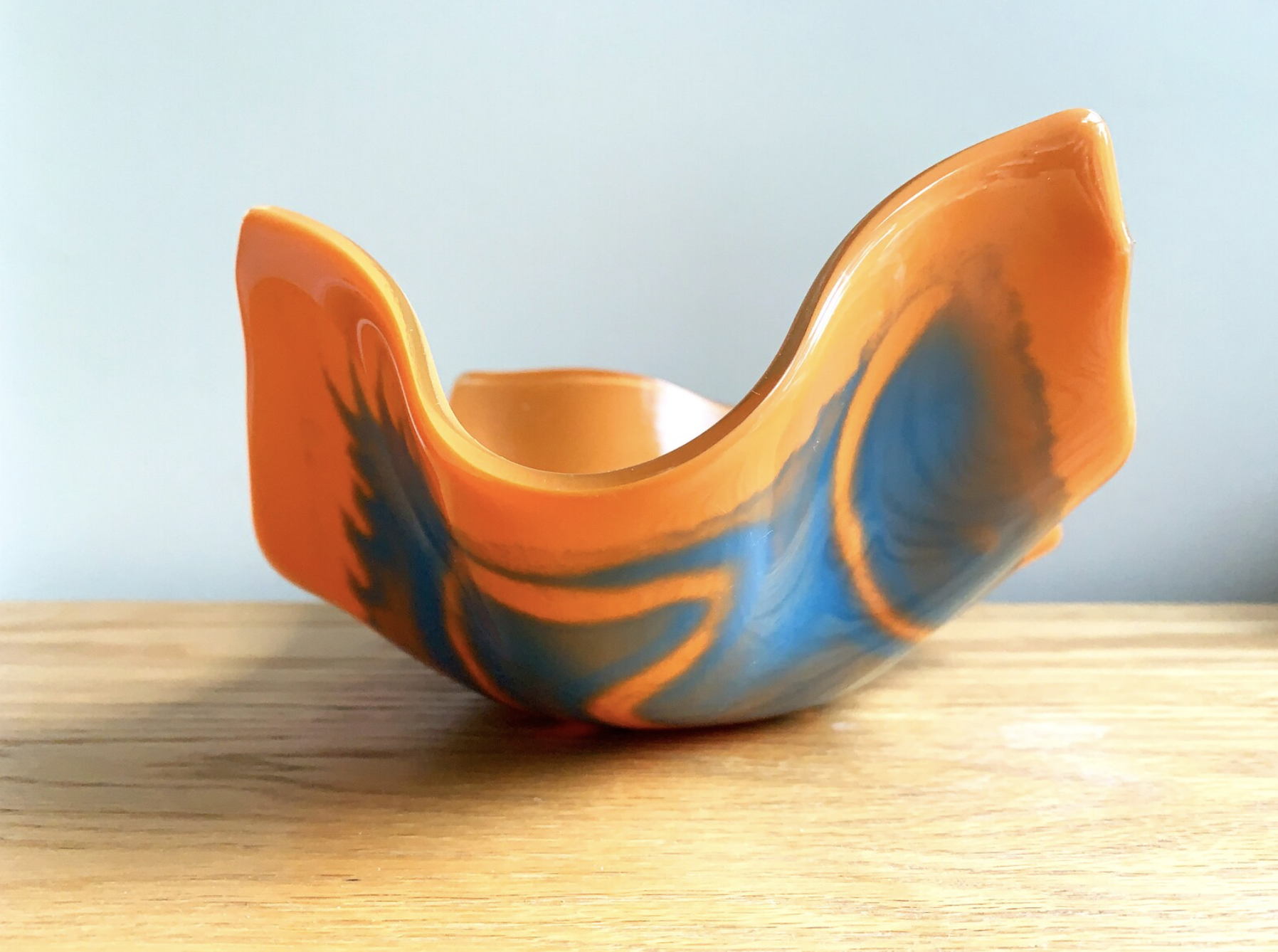 an orange and blue fused glass abstract bowl sits on a wooden tablen