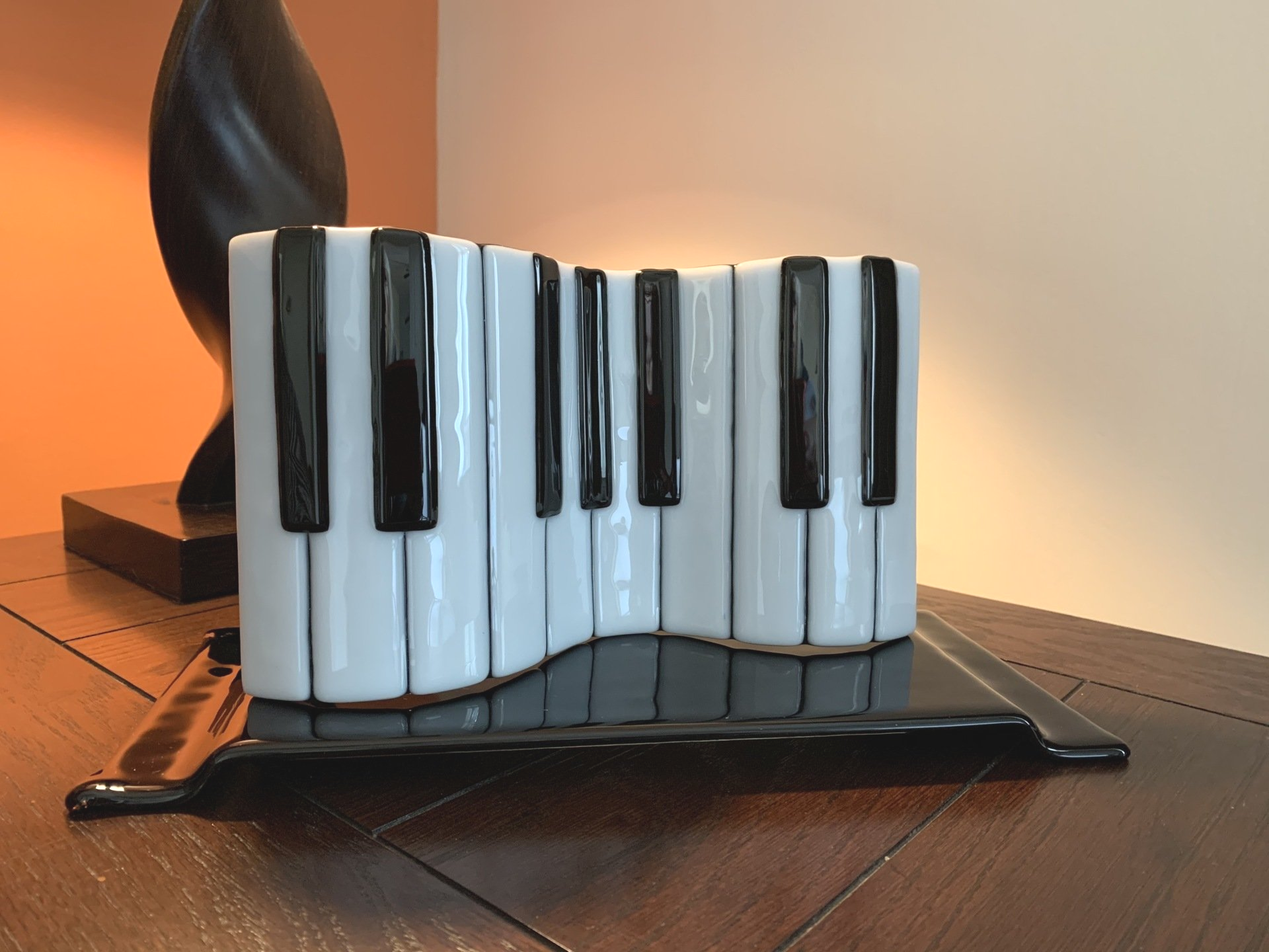 fused glass piano keyboard sculpture on a black stand sitting on an end table