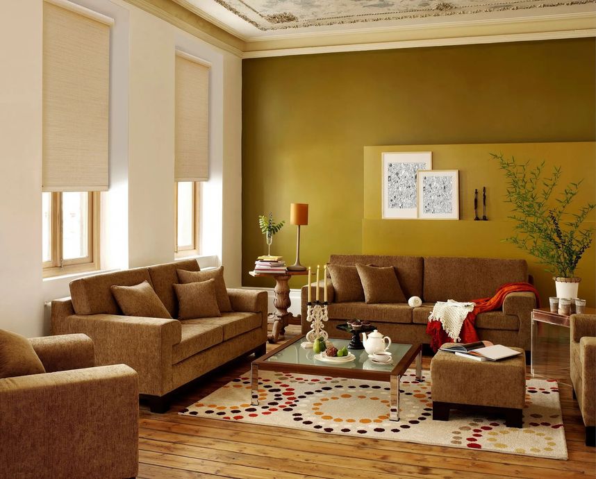A living room featuring brown sofas, a glass coffee table, a patterned area rug, and an olive green accent wall.