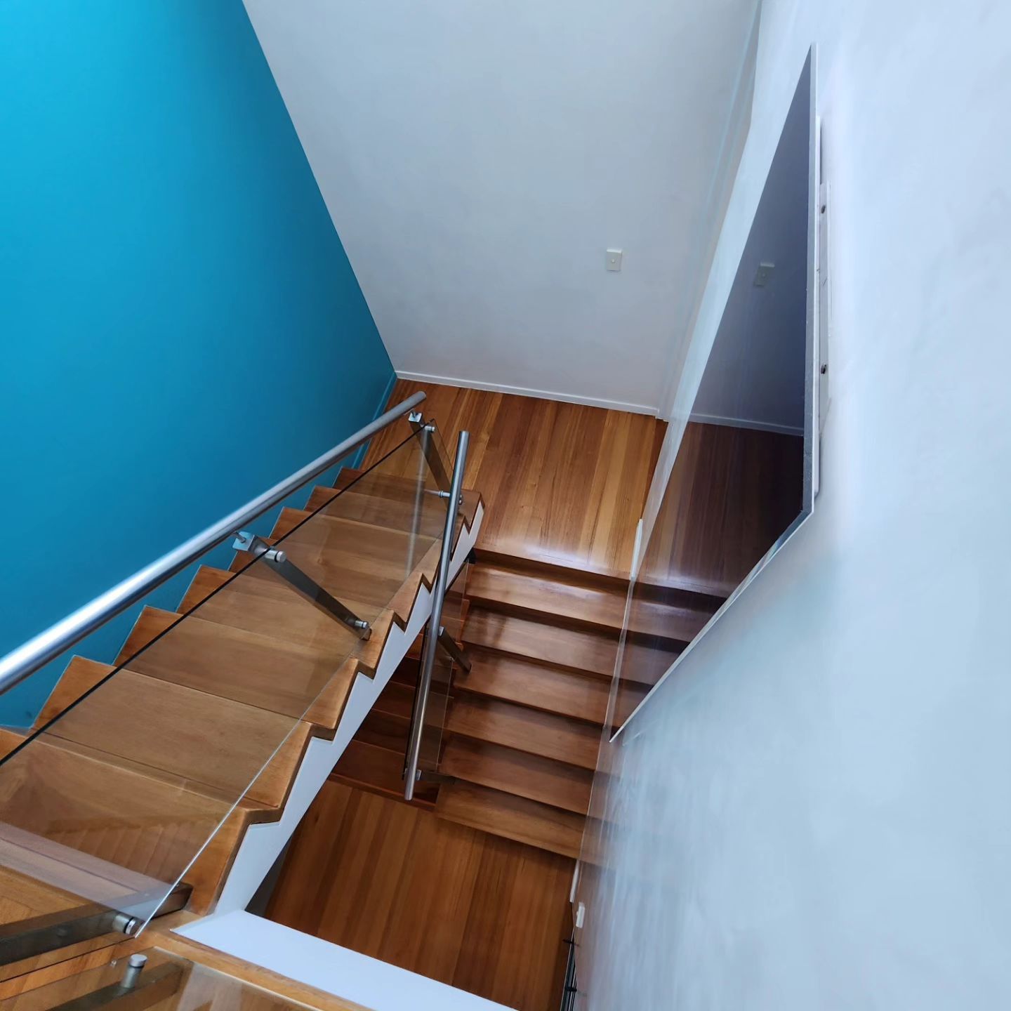 A Wooden Staircase With a Glass Railing and a Blue Wall — ATM Floors In Mount Louisa, QLD
