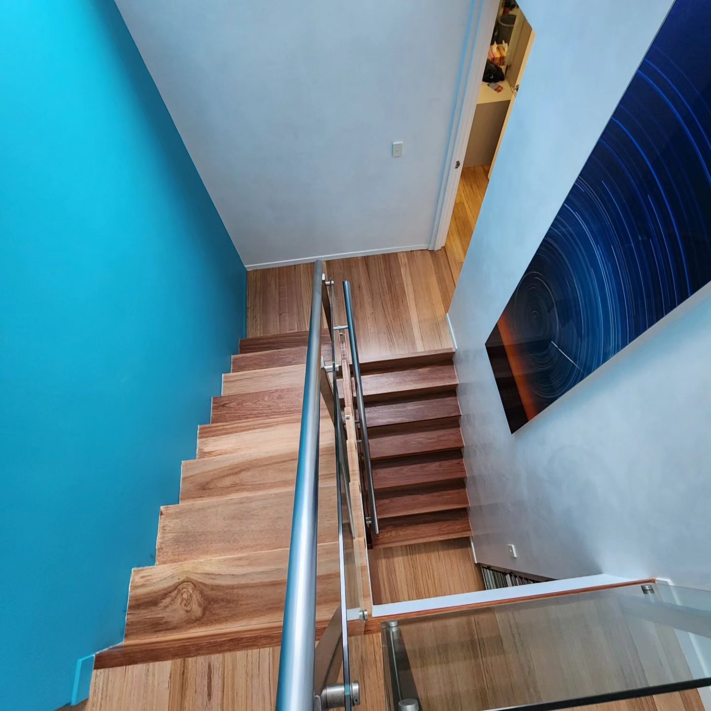 A Wooden Staircase With a Glass Railing and a Blue Wall — ATM Floors In Mount Louisa, QLD