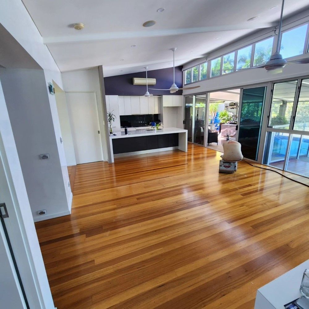 A Living Room With Hardwood Floors and a Kitchen in the Background — ATM Floors In Mount Louisa, QLD
