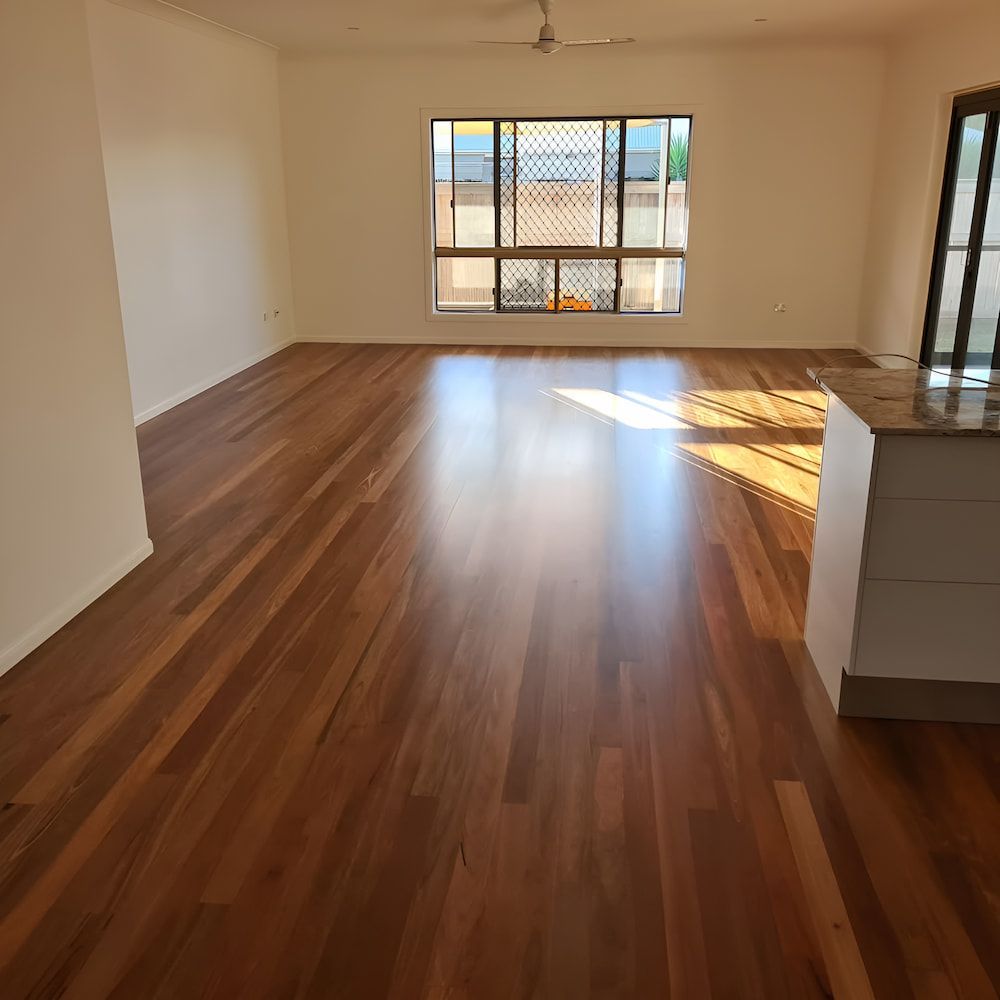 An Empty Living Room With Hardwood Floors and a Window — ATM Floors In Mount Louisa, QLD