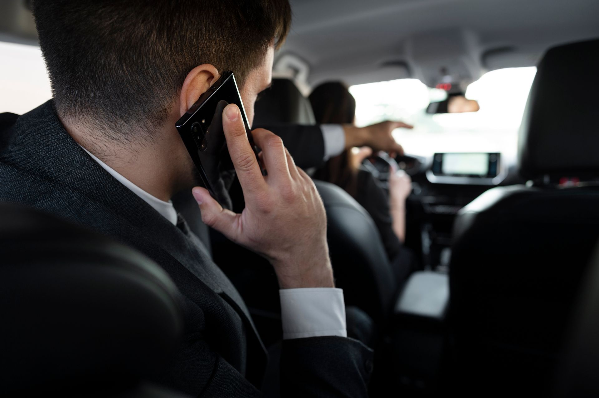 Man in suit talking on phone in car, other people present.