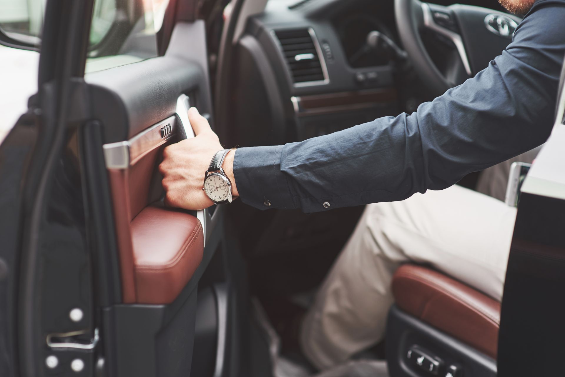 Person opening car door, wearing a watch. Interior features brown and black details.