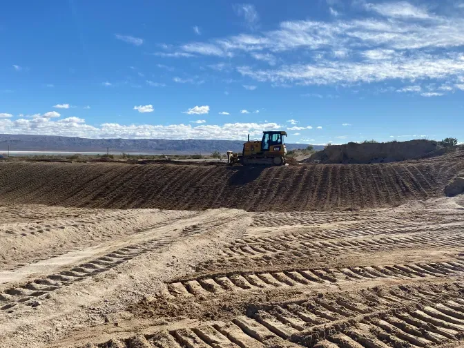 A bulldozer pushes dirt on a construction site. Blue sky, brown earth, and tire tracks.
