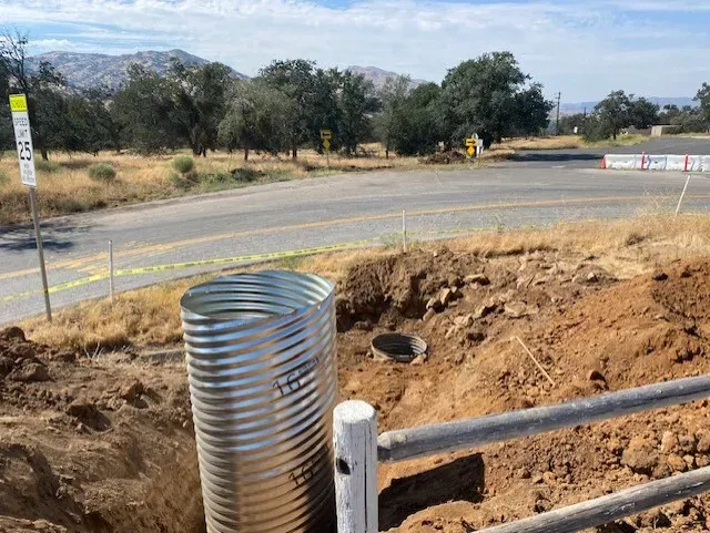 Corrugated metal culvert in a ditch next to a rural road, construction zone.