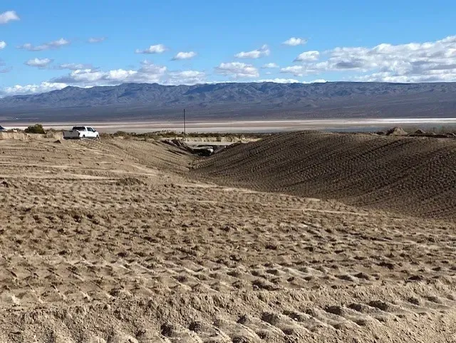 Dry, desert landscape with a dirt berm, a distant mountain range, and a white truck.
