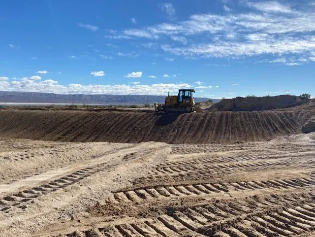 Bulldozer on a dirt embankment, desert landscape, sunny day.
