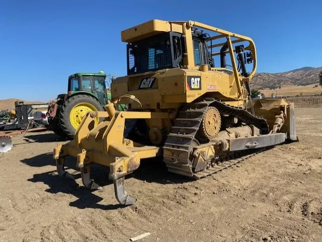 Yellow Caterpillar bulldozer on tracks, with a ripper attachment, parked outdoors on a sunny day.