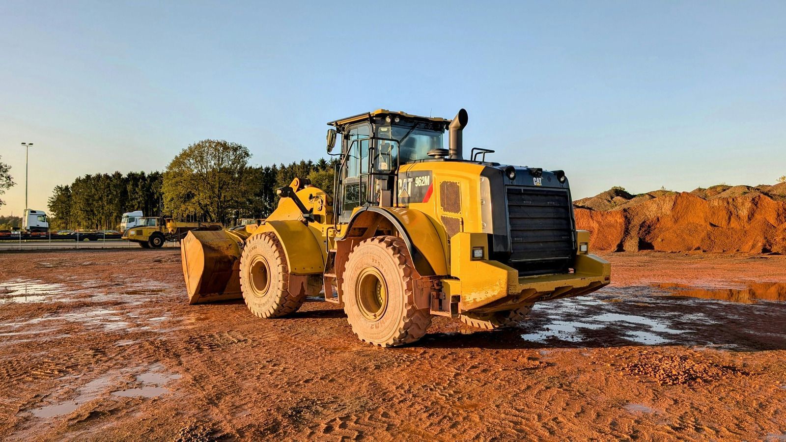 Construction workers installing green pipes in a trench next to a chain-link fence.