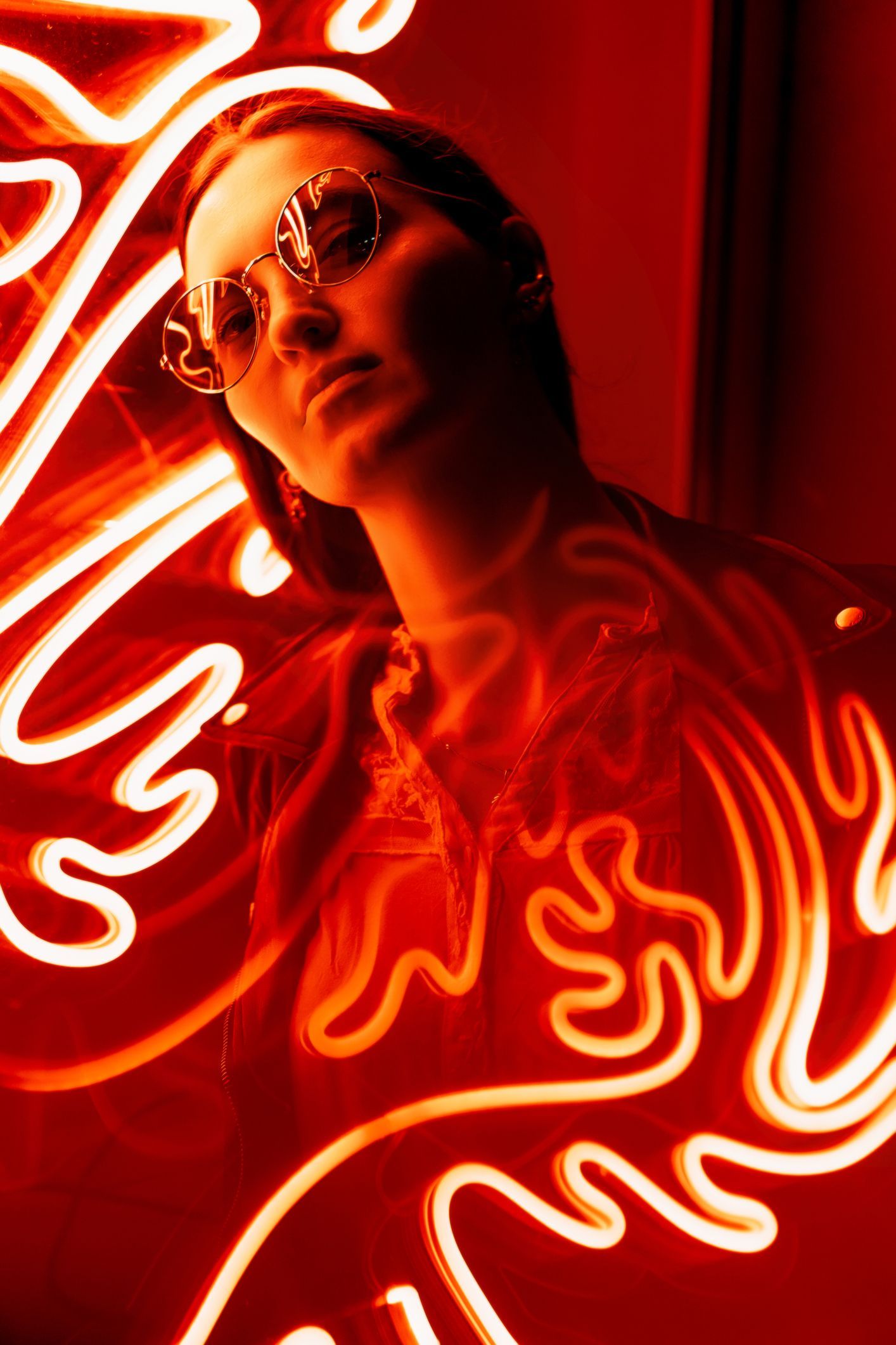 Woman in sunglasses, lit by red neon, with abstract glowing shapes surrounding her.