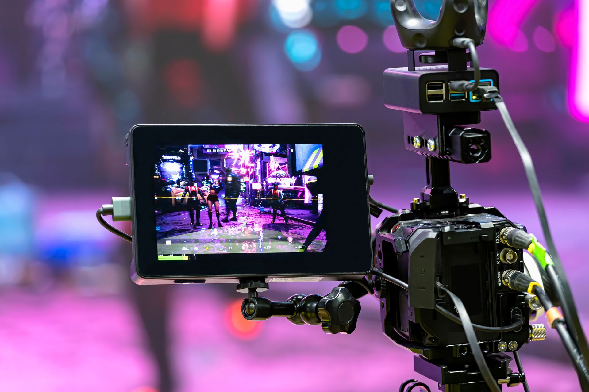 Camera with a monitor displaying a blurred scene of a brightly lit event. Pink and purple background.