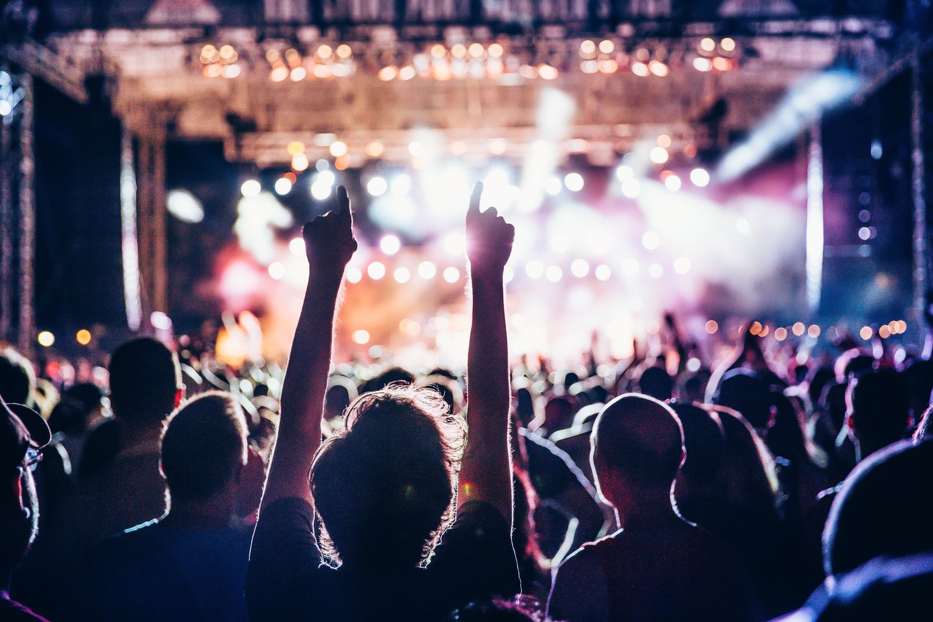 A crowd at a concert, arms raised in the air toward the stage, lit by bright lights and fog.