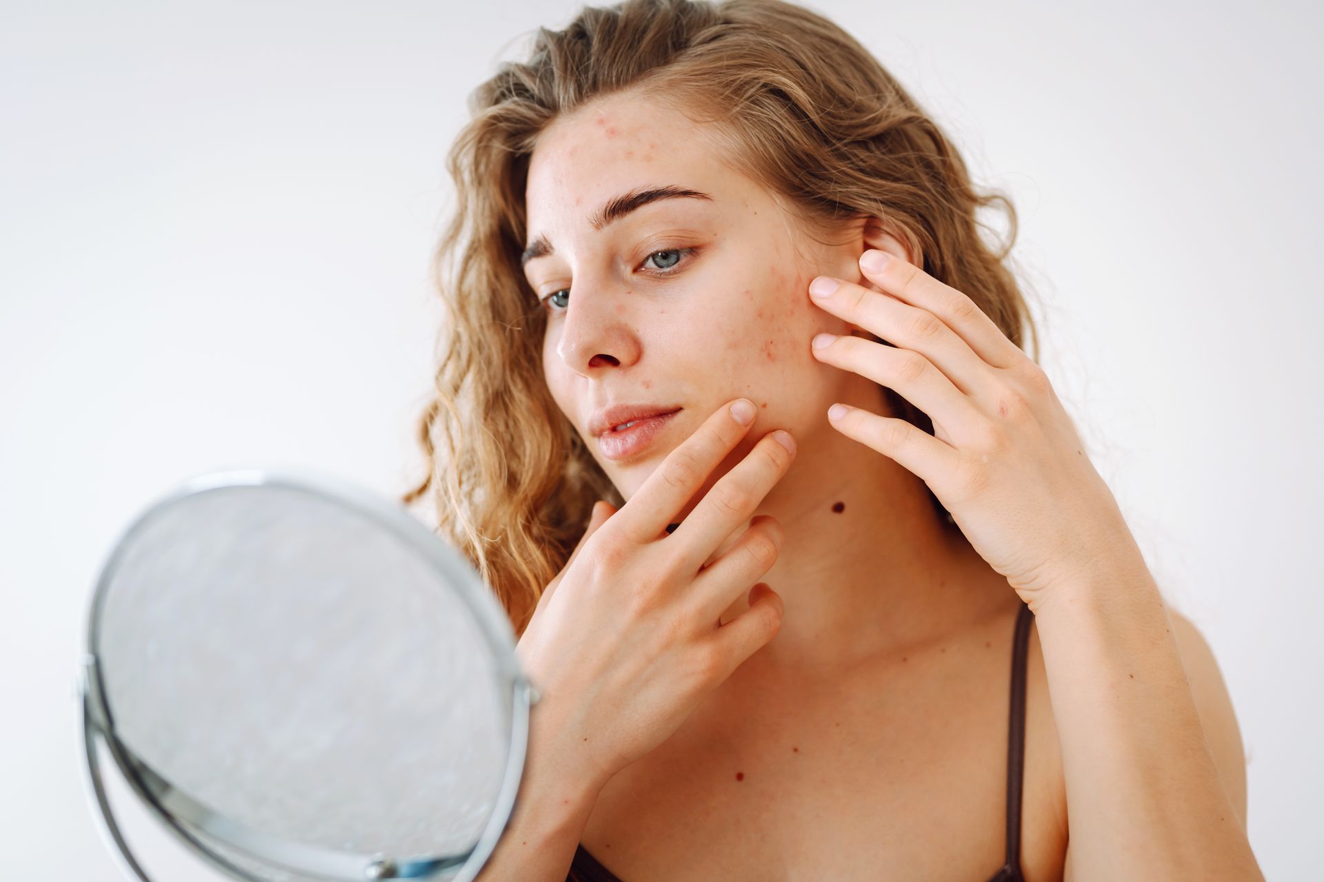 A woman is looking at her face in a mirror.