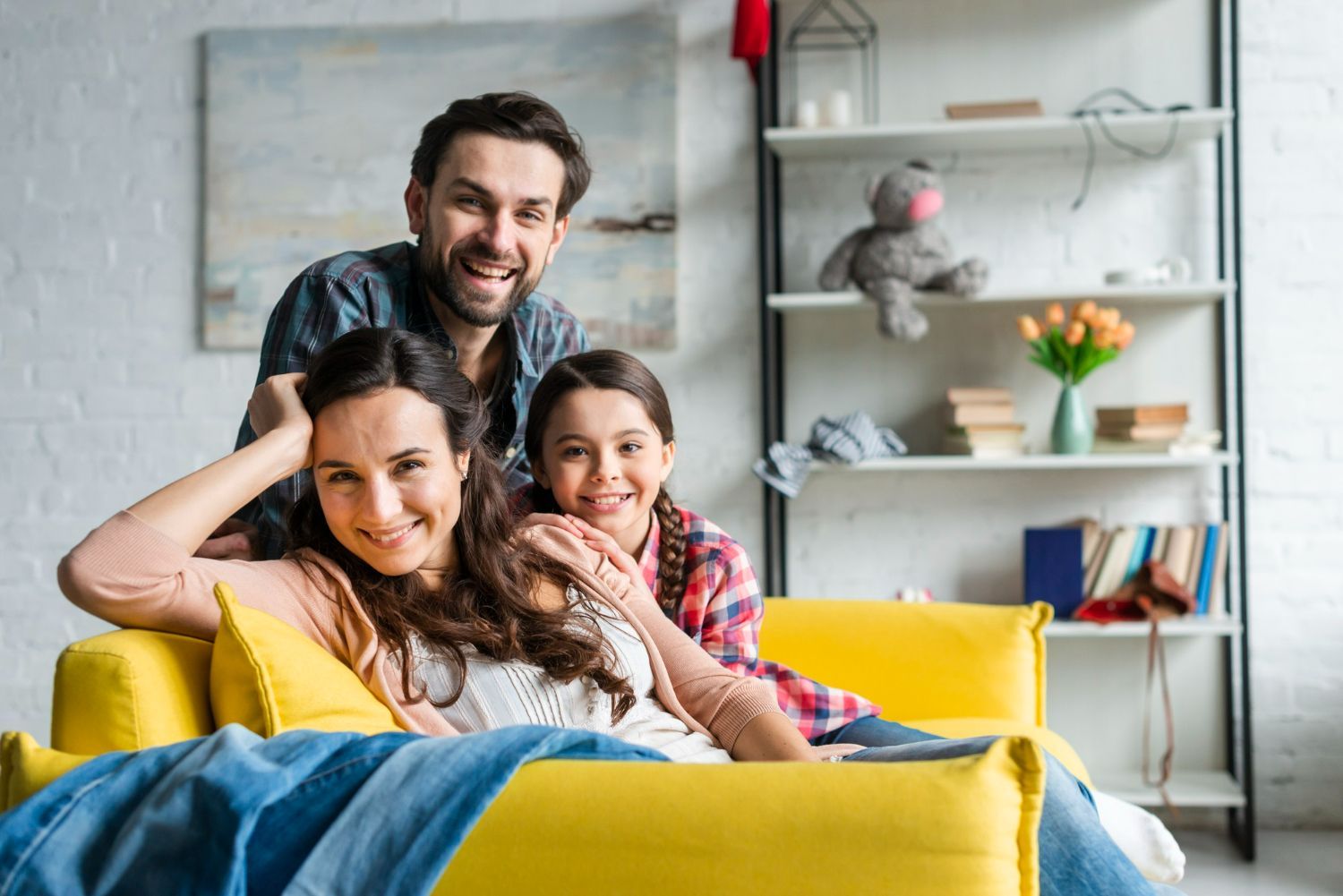 A family is sitting on a yellow couch in a living room.