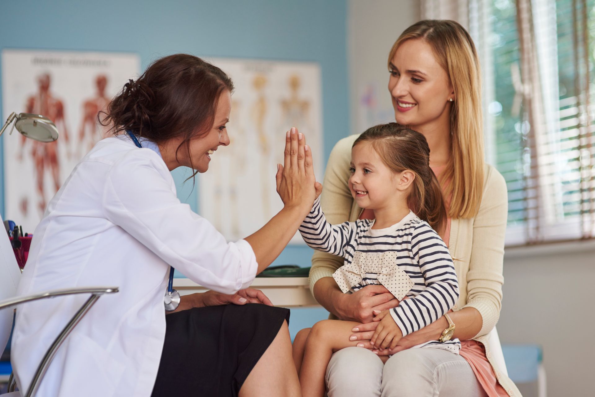 Doctor high-fives a young patient sitting on mother's lap in a medical office.